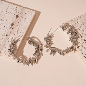 Detailed close-up of silver metal leaf tassel hoop earrings on textured beige stones