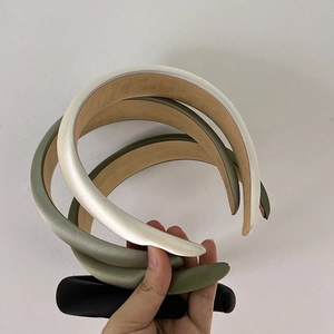 Close-up of three satin sponge headbands in beige, green, and black with velvet lining