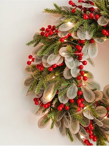 Detail of Christmas wreath featuring red berries, pine needles, and warm LED fairy lights