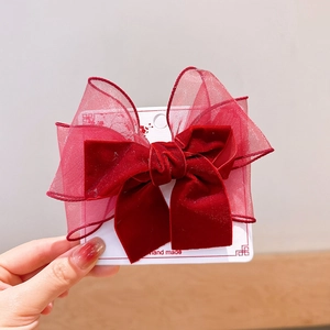 Detailed close-up of velvet and organza burgundy bow hair clip on a display card