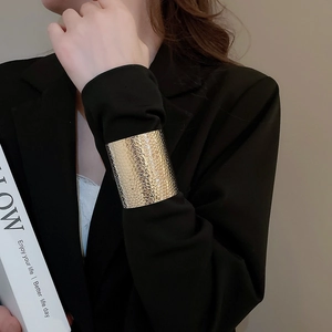 Close-up of wide gold metal cuff bracelet with hammered honeycomb texture on black blazer