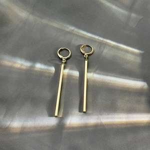 Close-up of minimalist gold long bar earrings on silk fabric showing metal texture