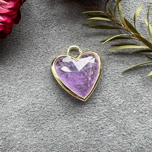 Detailed view of faceted heart-shaped purple crystal pendant with gold plating on felt
