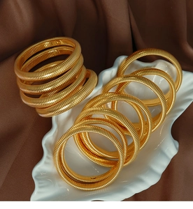 Detail of 10mm gold textured spiral bangles displayed on a white ceramic leaf tray