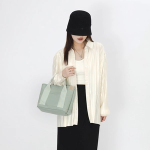 Detail of light green canvas tote bag showing stitching and front pocket on model