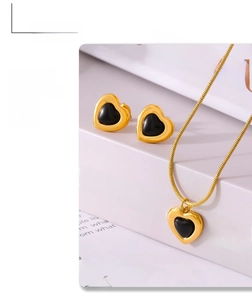 Close-up of gold heart jewelry set featuring black heart necklace and stud earrings