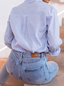 Detail view of a blue striped long sleeve shirt and ripped jeans from a back angle