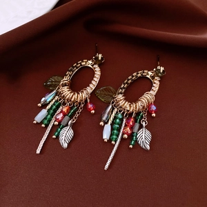 Detail shot of ethnic tassel earrings with green beads and hollow leaf pendants on velvet