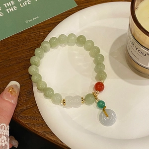Detail of beaded jade bracelet with平安扣 charm on a white porcelain dish and wooden table