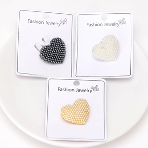 Three elegant heart-shaped pearl brooches in black, white, and gold on jewelry display cards