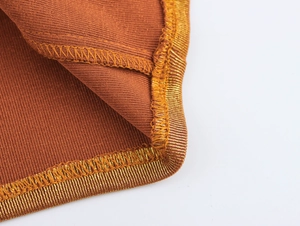 Détail de la texture tricotée marron et du bord cousu doré métallique de la robe courte