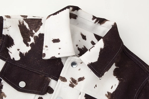 Detail of cow print cropped jacket featuring lapel collar and silver metal buttons