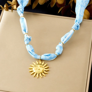 Macro view of gold sun face pendant on light blue patterned ribbon fabric necklace