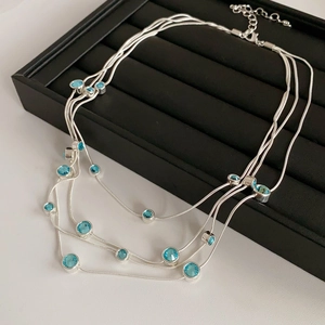 Close-up of layered silver snake chain necklace with blue zircons in a black jewelry box