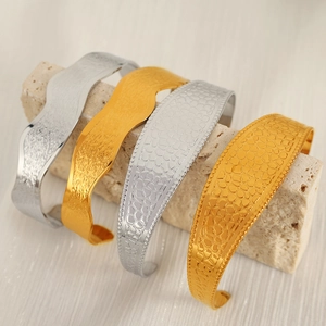 Textured ripple and honeycomb titanium steel cuff bracelets displayed on stone