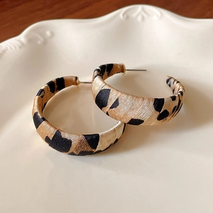 Detailed shot of leopard print fabric C-shaped hoop earrings on a vintage ceramic tray