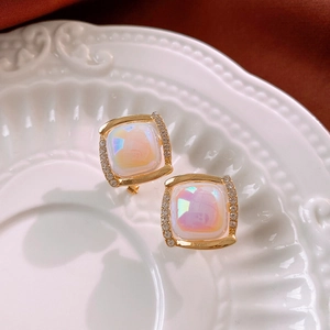 Macro view of gold square stud earrings with iridescent opal stones on a white ceramic plate