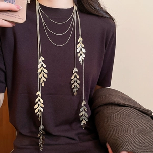 Detailed view of layered gold leaf tassel necklace styled on a brown sweater