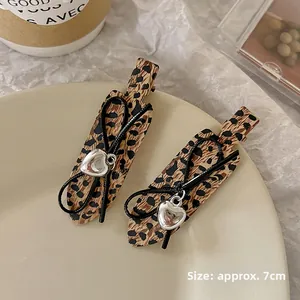 Detailed view of 7cm leopard print bow hair clips with silver heart pendants on a plate