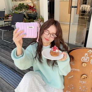 Chic pink striped canvas makeup pouch held by a woman in a trendy cafe setting