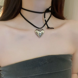 Detail of a black velvet choker featuring a polished silver heart pendant on a model