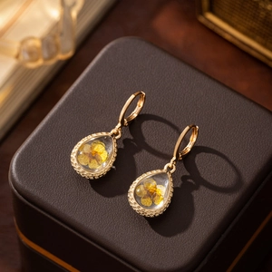 Macro shot of gold teardrop earrings with real yellow dried flowers in clear resin