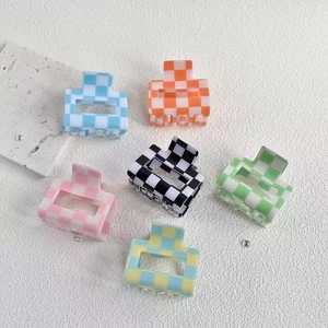 Detailed top view of various colorful checkered hair claws on a minimalist marble background