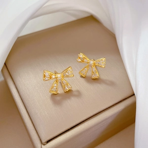 Macro view of gold bow earrings with white zircons on a champagne jewelry box surface