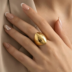Detailed macro shot of a gold chunky shield ring worn on a model hand with fabric backdrop