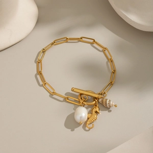 Close-up of gold paperclip chain bracelet with pearl, seahorse and shell charms