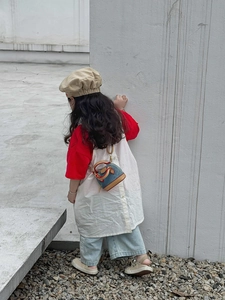 Kind trägt eine Muschel-Umhängetasche aus Denim und Leder vor einer Betonwand