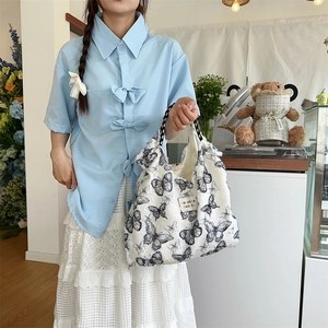 Detail of canvas tote bag featuring black butterfly patterns and fringe tassel trim