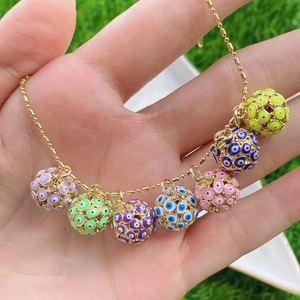 Nahaufnahme eines goldenen Armbands mit bunten Evil-Eye-Anhängern auf grünem Gras