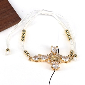 Detail of cross charm with clear crystals on white adjustable braided rope bracelet