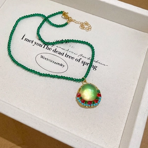 Detail view of a vintage crystal beaded necklace with a green resin pendant and gold metal