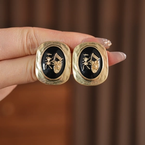 Close-up of vintage oval gold earrings with black enamel and embossed carriage detail