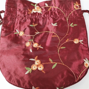 Detailed view of floral embroidery on a wine red satin drawstring bucket bag
