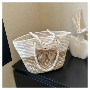 Detail of woven tote bag with champagne bow and white rope handle on a dark surface