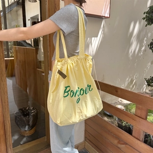 Detail of light yellow canvas tote bag with green Bonjour print and drawstring closure