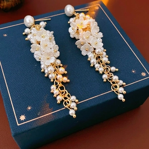 Close-up of resin flower earrings with long pearl tassels on a blue jewelry box