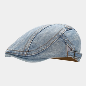 Detail of washed denim flat cap showing bronze buckle and brown contrast stitching