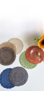 Detail of round woven cotton placemats in deep blue, grey, and orange with braided edges
