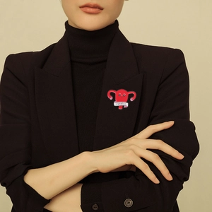 Detailed view of an enamel uterus pin with Cuterus text pinned on a black suit lapel