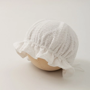 Close-up of white cotton lace baby bonnet with floral embroidery and ruffle brim
