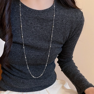Detail of silver layered beaded long tassel necklace on a grey ribbed sweater