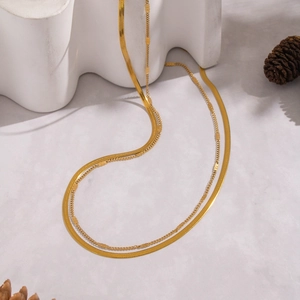 Double-layered golden snake chain necklace draped on a white wavy prop with pine cones