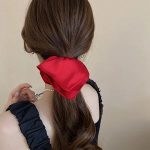 Macro shot of red satin bow scrunchie with pearlescent shine on wavy brown hair