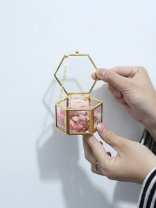 Detail of a gold hexagonal glass jewelry box with pink dried flowers and a silver ring