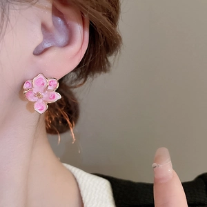 Elegant pink enamel flower stud earrings with gold plating shown on a model's ear