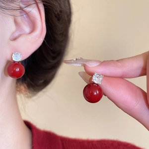 Detailed close-up of a vintage red pearl stud earring with a sparkling rhinestone accent